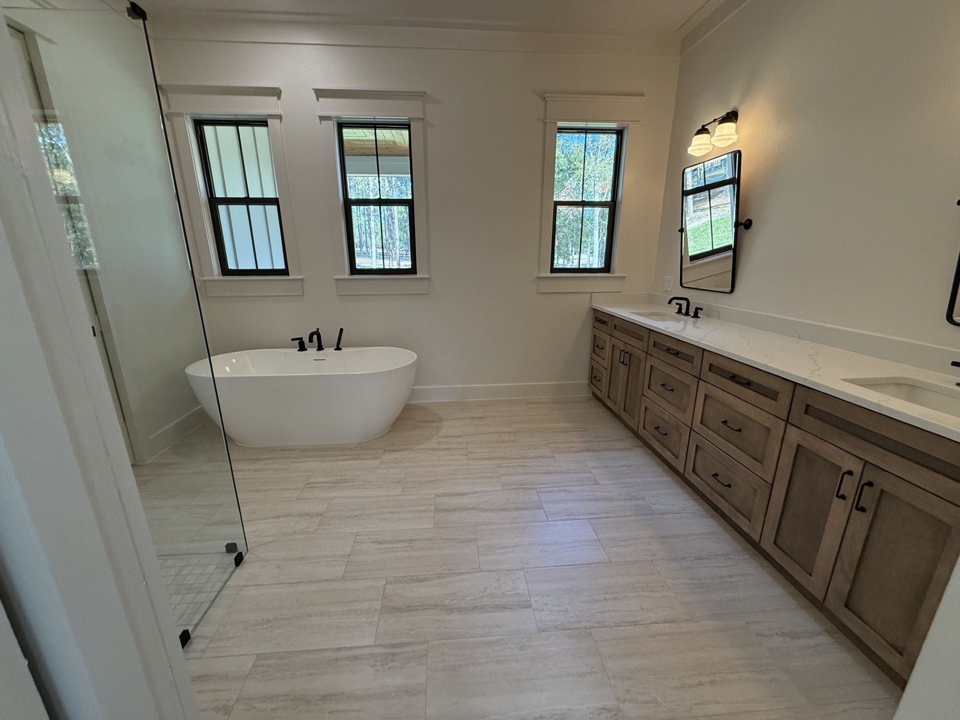 Modern bathroom with freestanding tub, double vanity, light wood flooring, and three windows