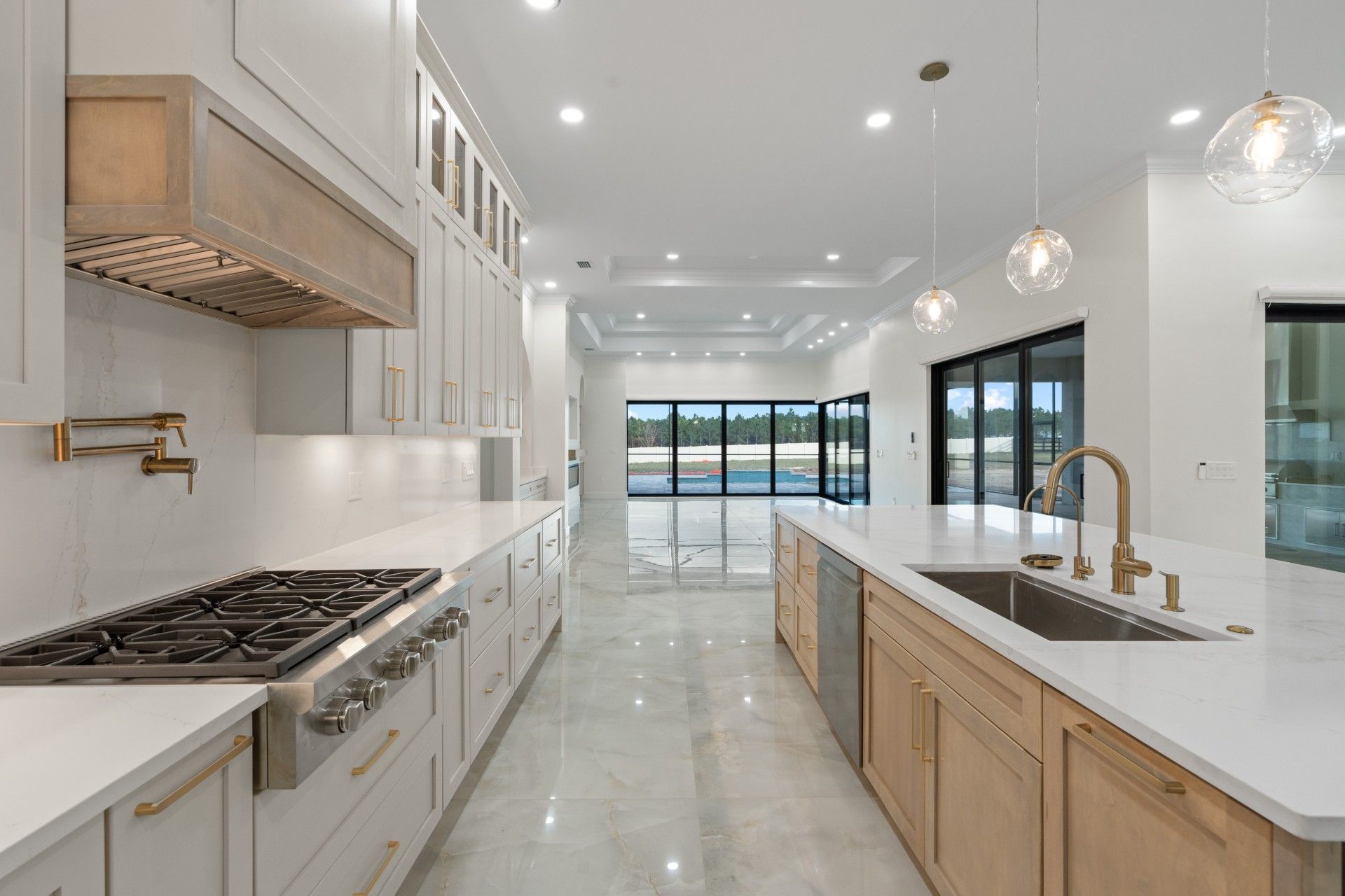 Bright modern kitchen with white countertops, light wood cabinets, stainless stove, and island sink
