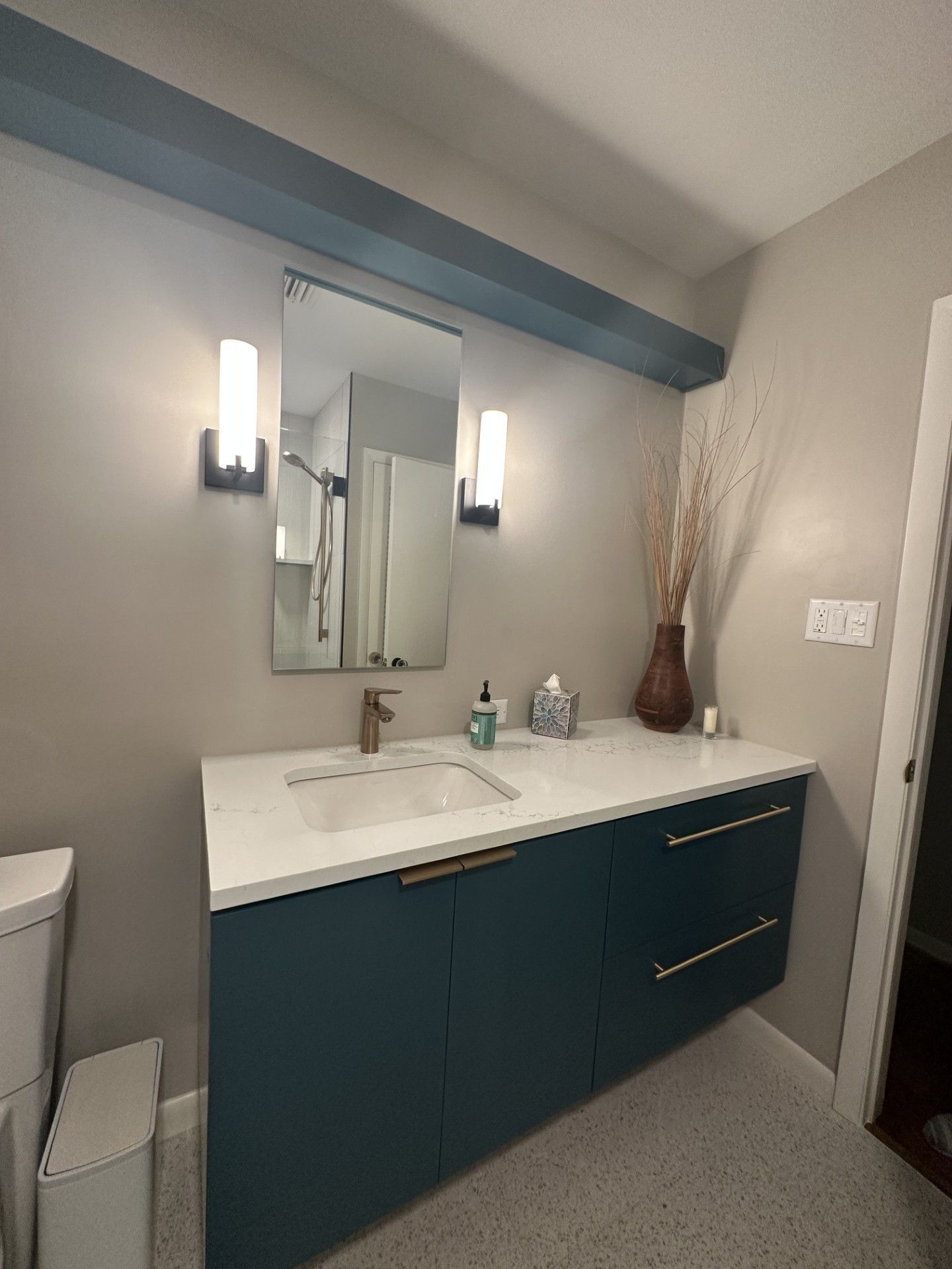 Modern bathroom vanity with teal cabinets, white countertop, mirror, and wall sconces