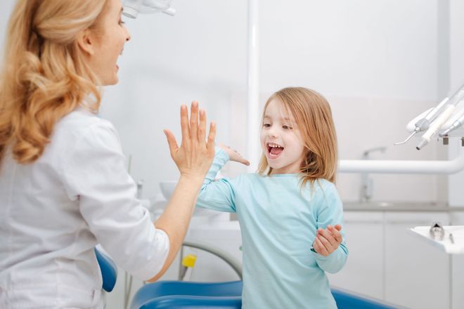 Dentist high-fives a happy child in a dental office.
