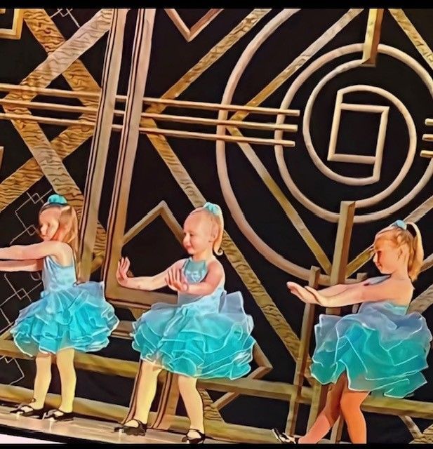 Three young girls in turquoise ruffled dresses dance on a stage with an art deco background.