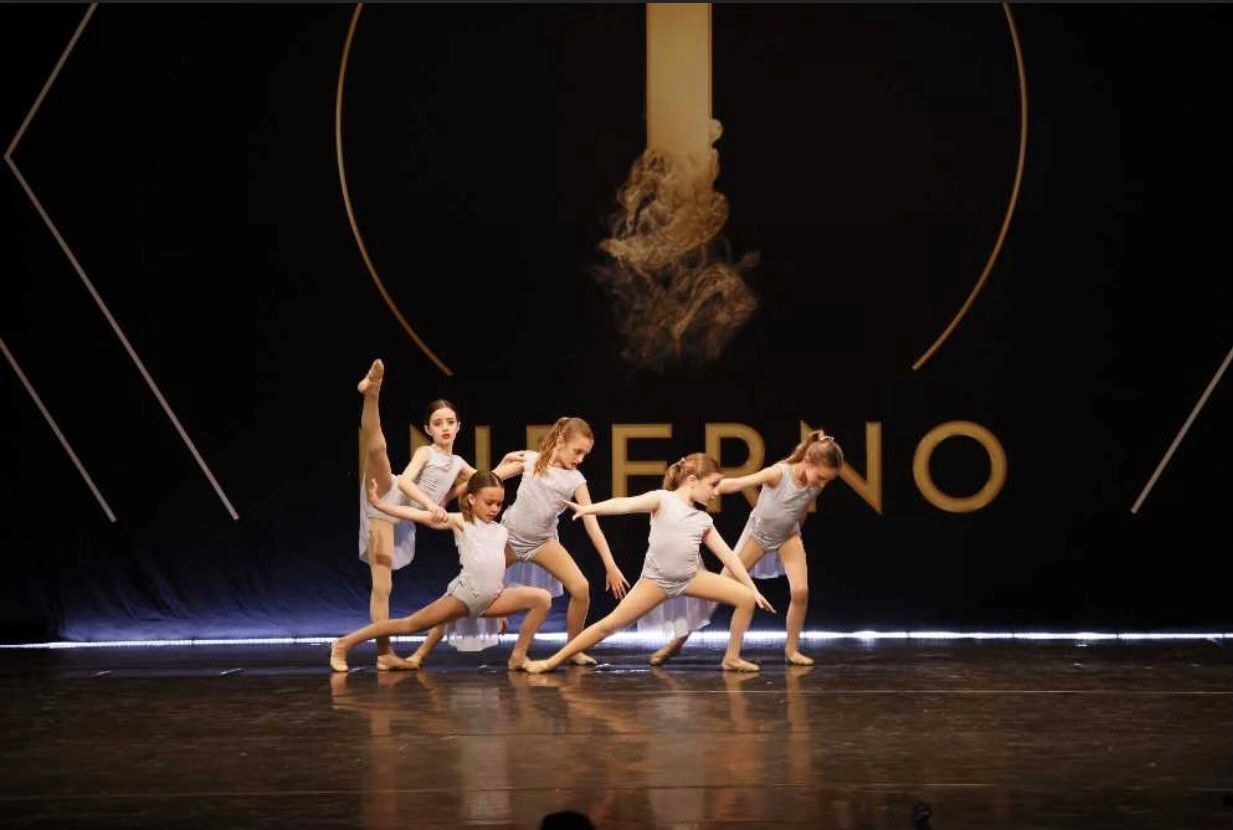 Five young dancers on stage in grey leotards, performing a routine