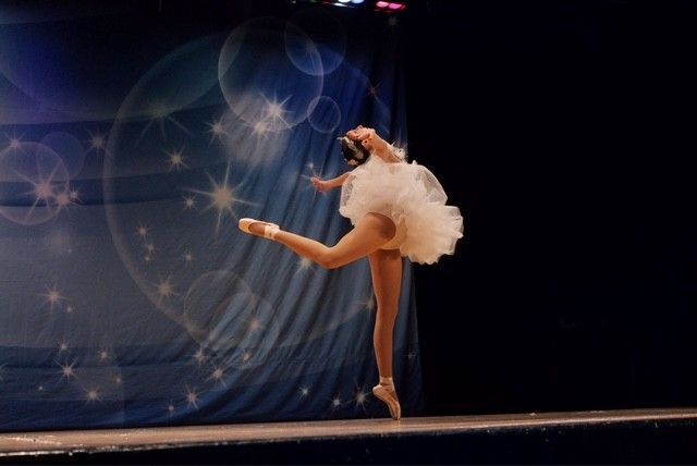 Ballerina in a white tutu, arched back, en pointe on a stage with a starry backdrop.