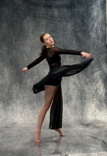 Woman in black dance attire spins gracefully in a studio against a mottled gray backdrop.