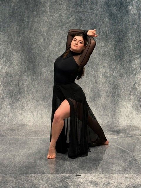 A dancer in a black dress with a high slit poses gracefully against a gray backdrop.