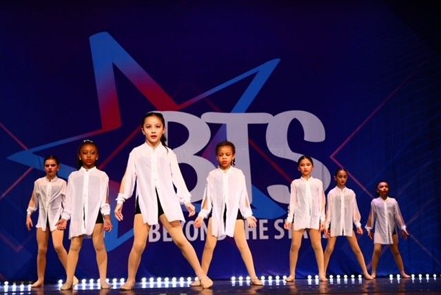 Young dancers in white shirts and black shorts perform on stage