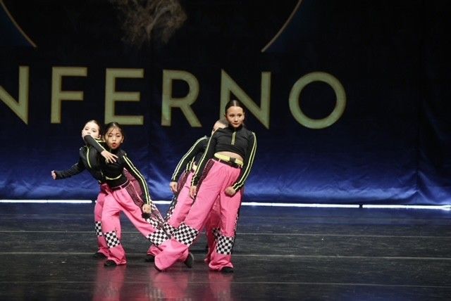 A group of young dancers in matching pink and black outfits perform on a stage