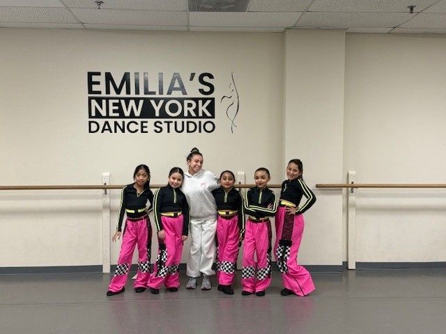 Group of young dancers in pink and black outfits posing with an instructor at Emilia's New York Dance Studio.