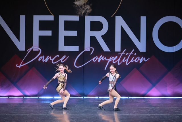 Two dancers in gold costumes performing onstage at Inferno Dance Competition