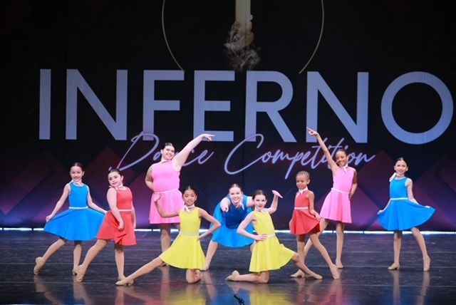 Dance troupe in colorful costumes on stage before an “INFERNO” backdrop