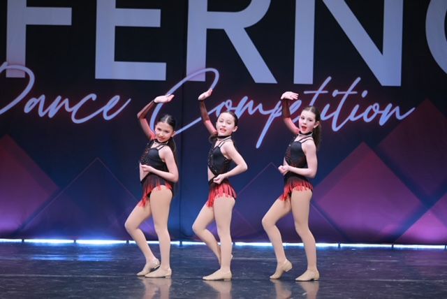 Three dancers in black and red costumes posing on a stage at a dance competition