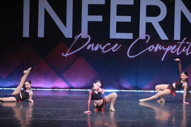 Three dancers pose on a stage under an INFERNO Dance Competition backdrop.