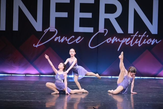 Three dancers in purple costumes pose on a stage at Inferno Dance Competition.