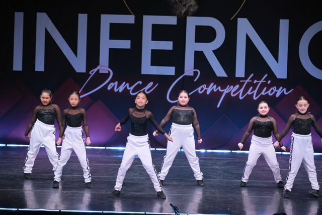 Five dancers in white pants performing onstage under an INFERNO Dance Competition backdrop