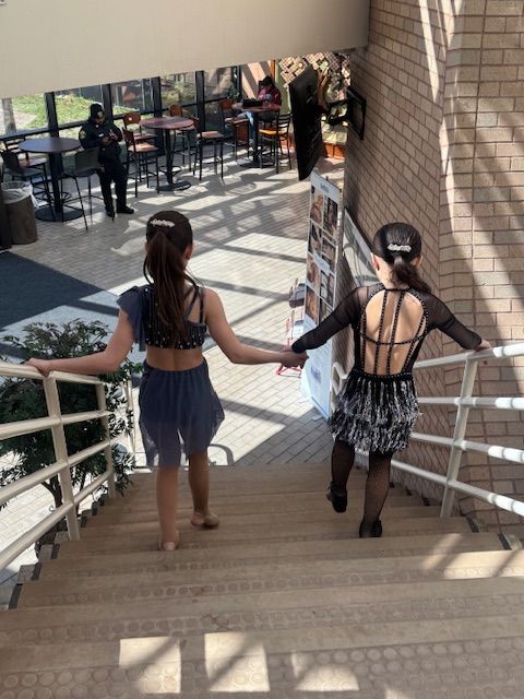 Two people holding hands while walking down outdoor stairs in a sunlit courtyard