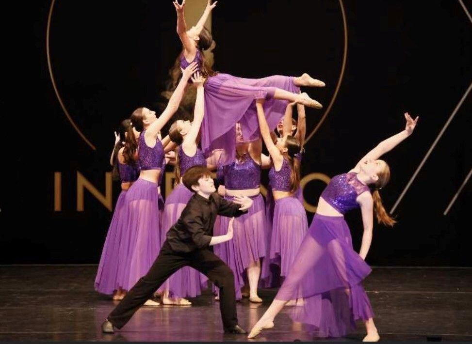 A dance troupe in purple costumes performs on stage. Dancers lift one another, creating a dynamic human pyramid.