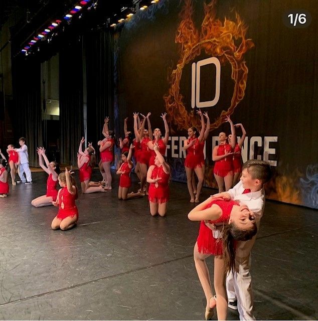 A group of dancers in red outfits performing on stage, one dancer is held in a lift.