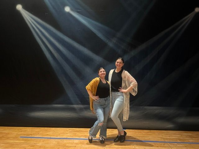 Two people pose together on a stage under bright spotlight beams.