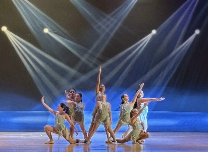 Dancers in gold costumes pose on a blue-lit stage under dramatic spotlights.