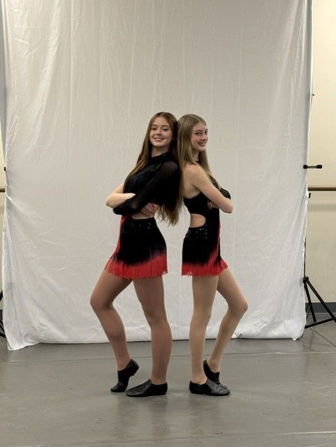 Two dancers in black-and-red costumes pose back-to-back in a studio with a white backdrop.