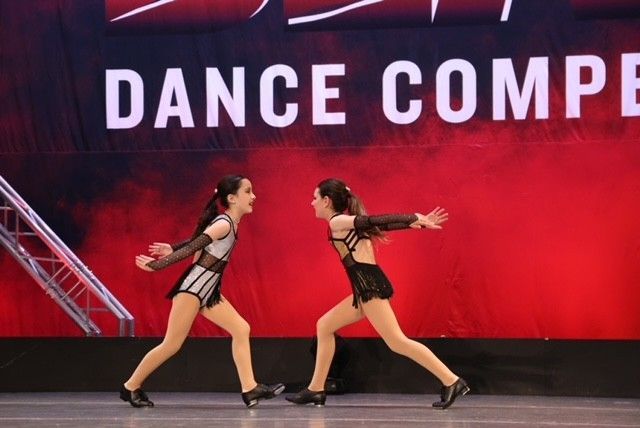 Two dancers in black and red costumes performing onstage before a red
