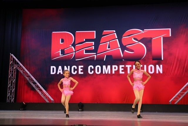 Two dancers onstage before a red BEAST Dance Competition backdrop