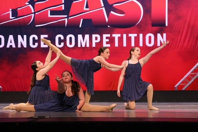 Four dancers in blue costumes pose on stage at a dance competition with a red “BEAST” backdrop
