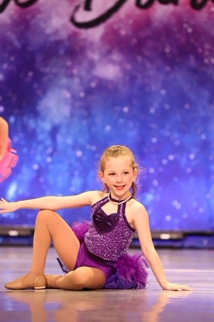 Young dancer in a purple costume posing on stage against a sparkling blue backdrop