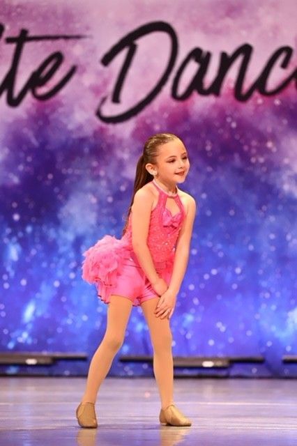 Young dancer in a bright pink costume posing on stage with a purple backdrop