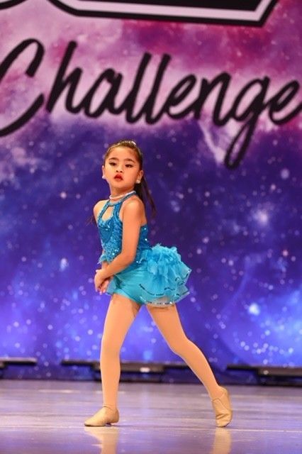 Young dancer in a blue costume posing on stage in front of a purple