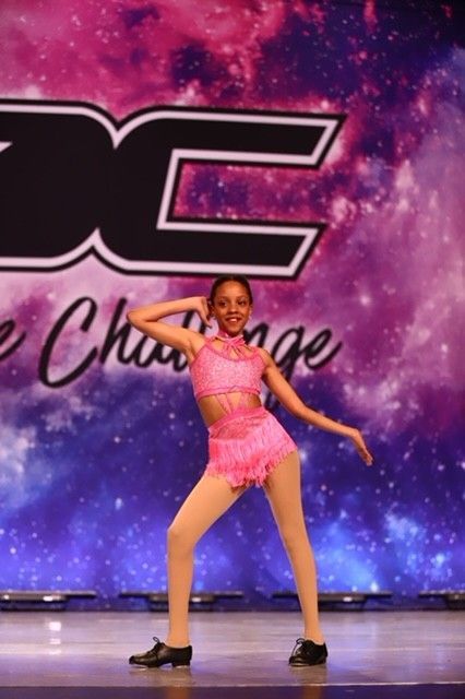 Young dancer in pink costume posing on a competition stage with a purple galaxy backdrop