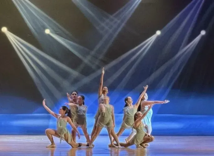 Dancers in beige costumes pose on a stage under blue lighting and white spotlights