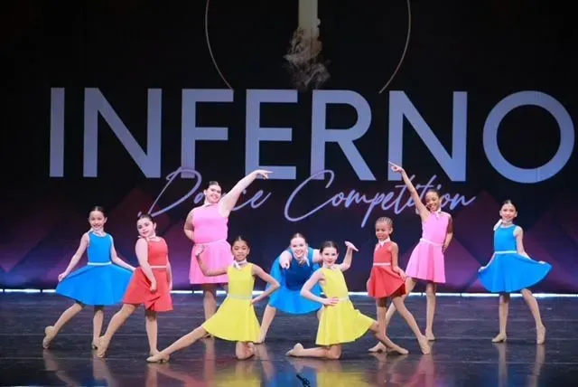 Dancers in colorful costumes pose onstage before a large “INFERNO” backdrop.