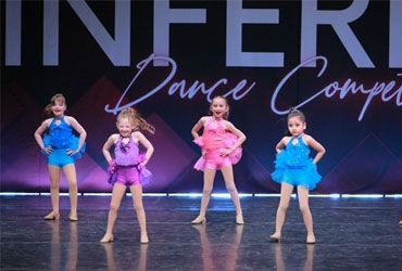 Four young dancers in bright blue and pink costumes on a stage at a dance competition