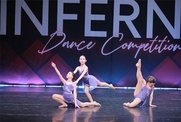Three dancers in purple costumes pose on stage at an Inferno Dance Competition backdrop