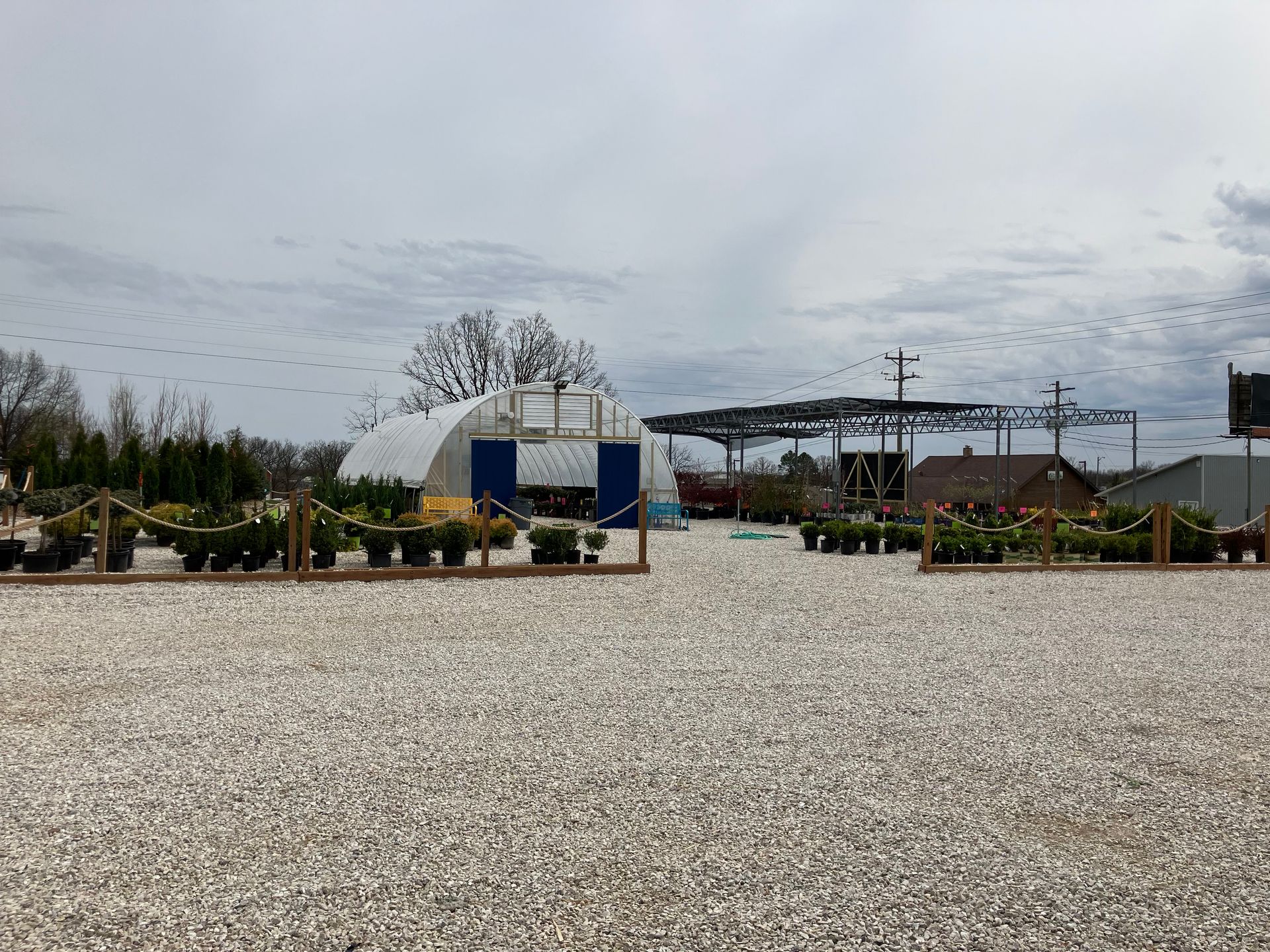 A gravel lot with a building in the background and a lot of potted plants in the foreground.