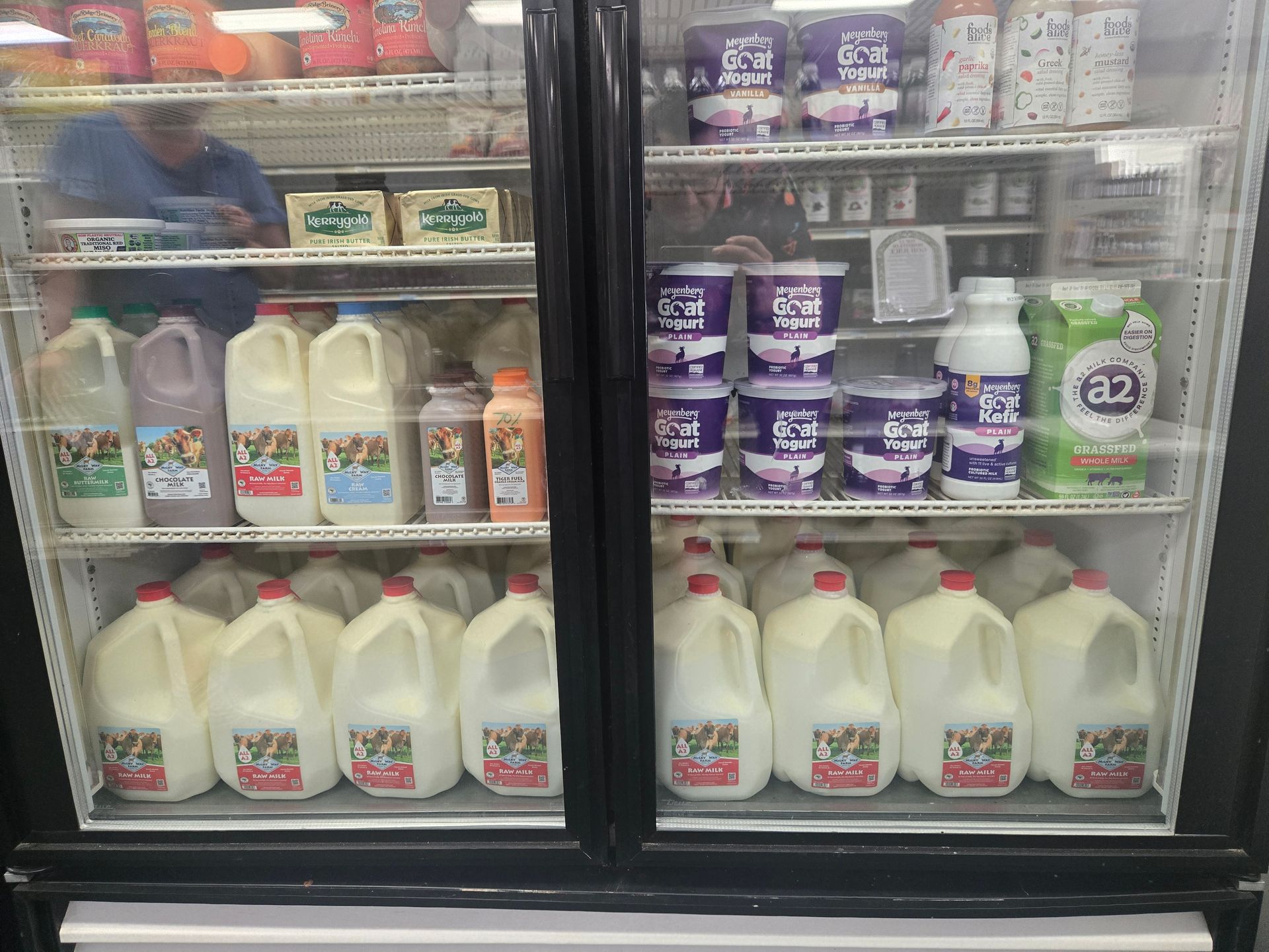 Two glass-front refrigerators filled with various brands and sizes of milk jugs, cartons, and dairy tubs.