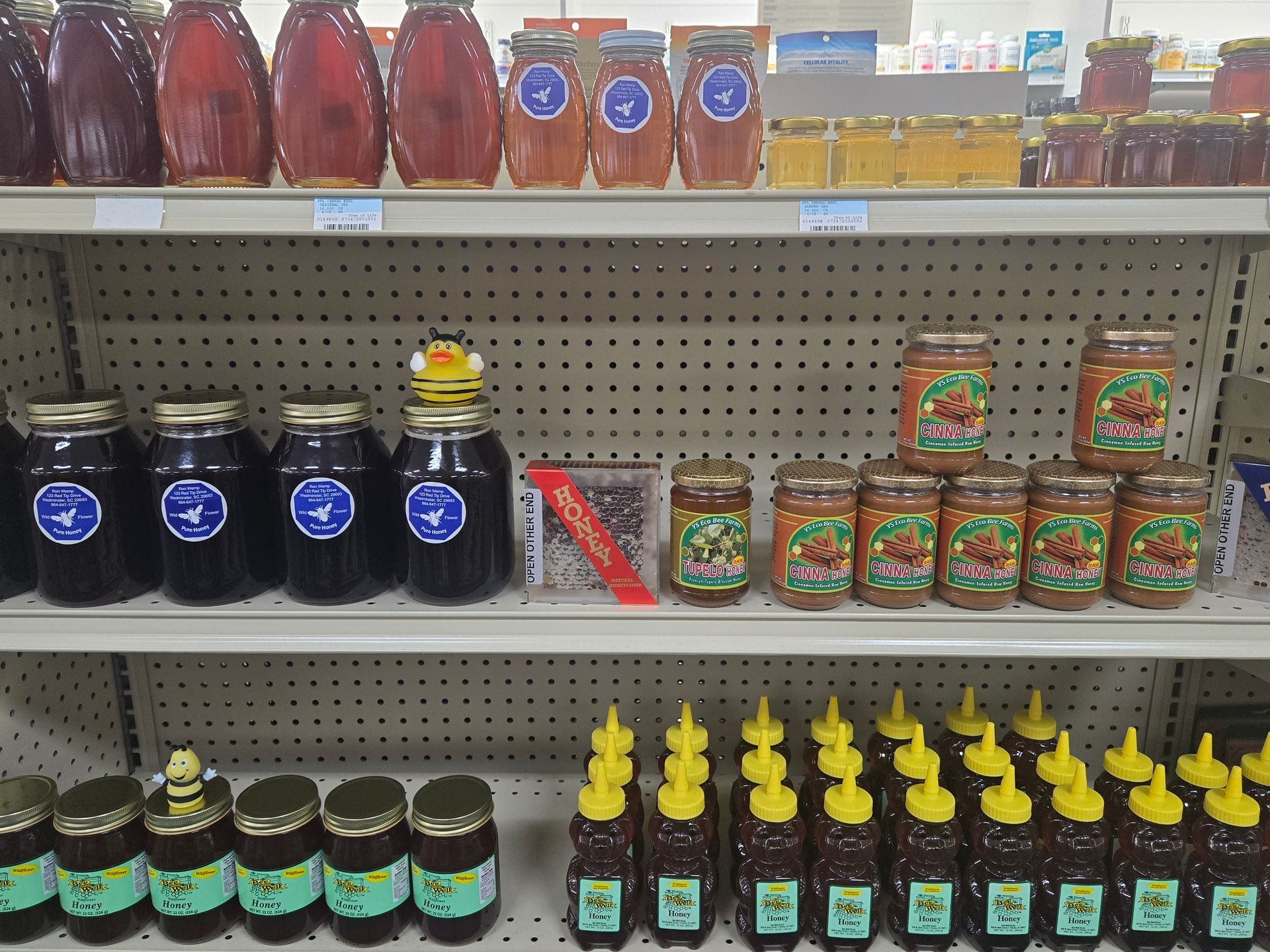 Three shelves in a grocery store display various sizes and brands of honey in glass jars and squeeze bottles.