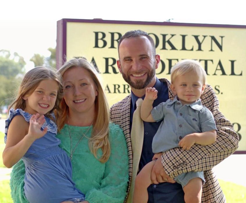 A family poses in front of a brooklyn dental sign