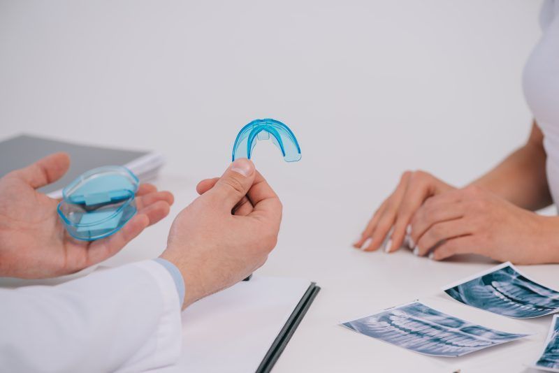 A dentist is holding a blue mouth guard in front of a patient.