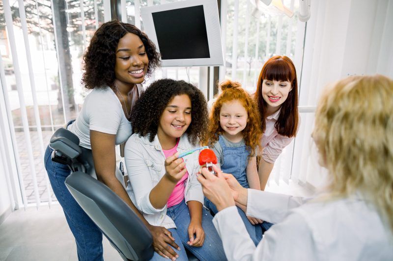 A group of women and children are sitting in a dental chair talking to a dentist.