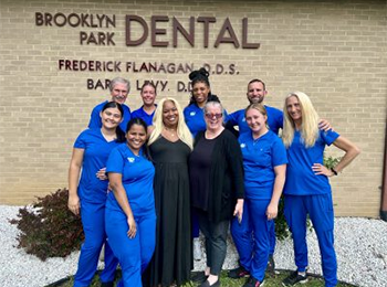A group of people posing for a picture in front of a brooklyn park dental sign.