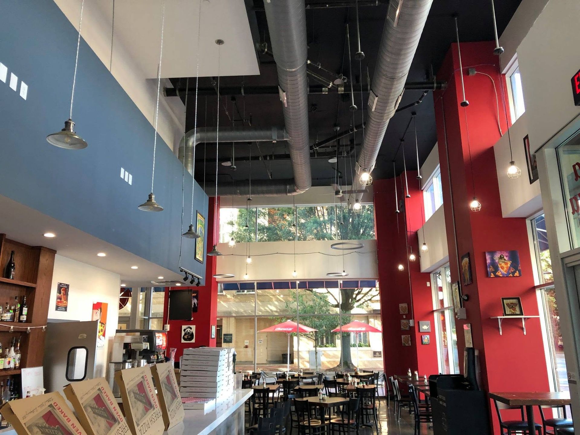 Spacious modern café interior with high ceilings, red and blue walls, tables, and hanging lights