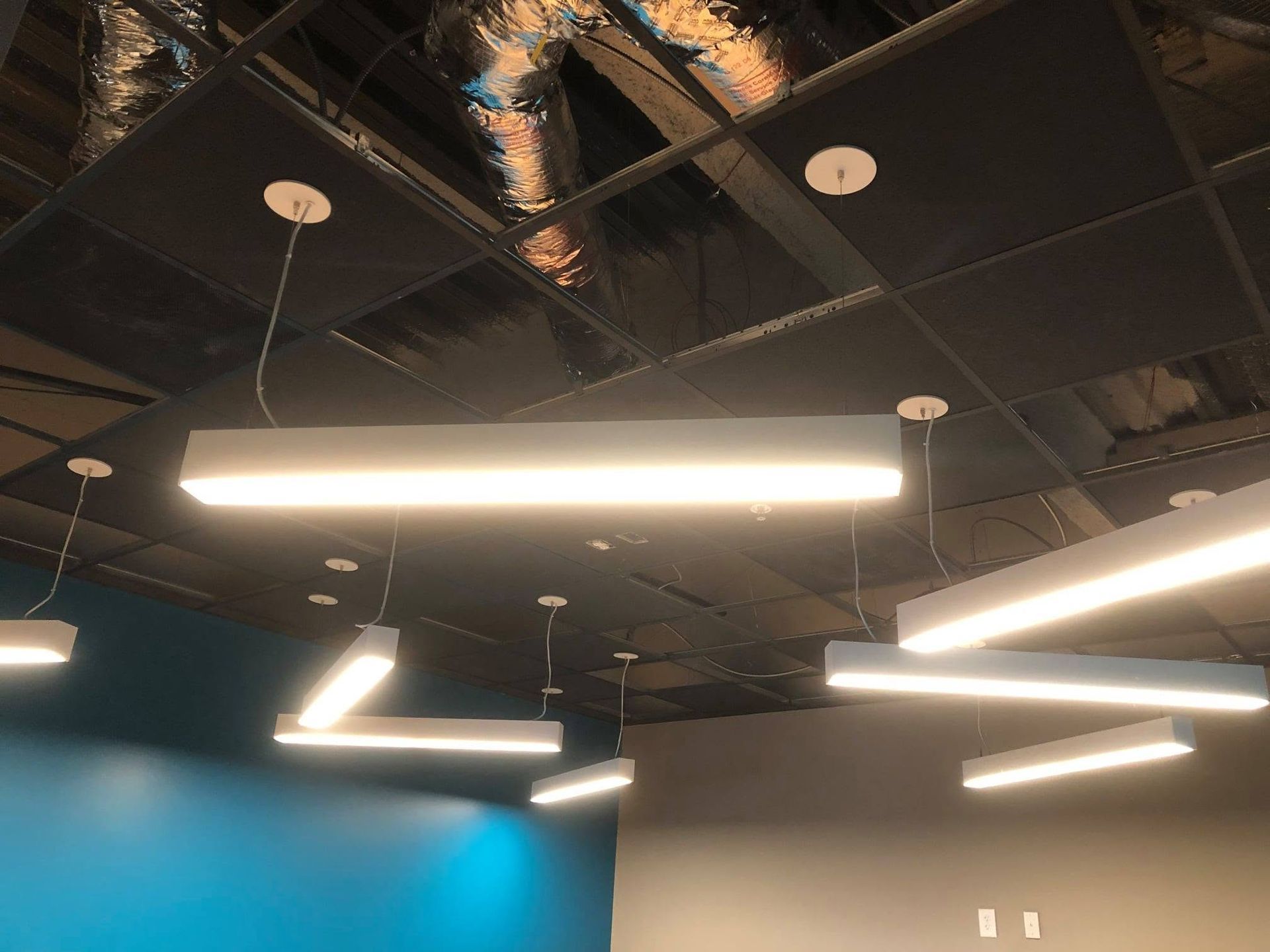 Ceiling with hanging fluorescent light fixtures and exposed dark ceiling panels