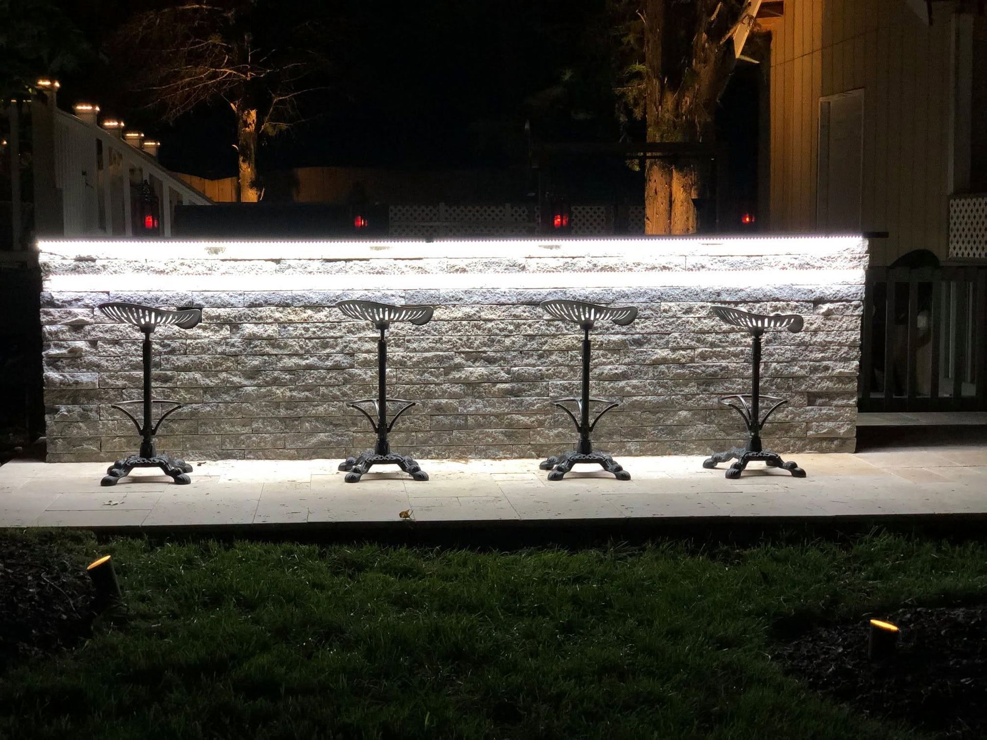 Illuminated outdoor bar with stone front and three black stools at night