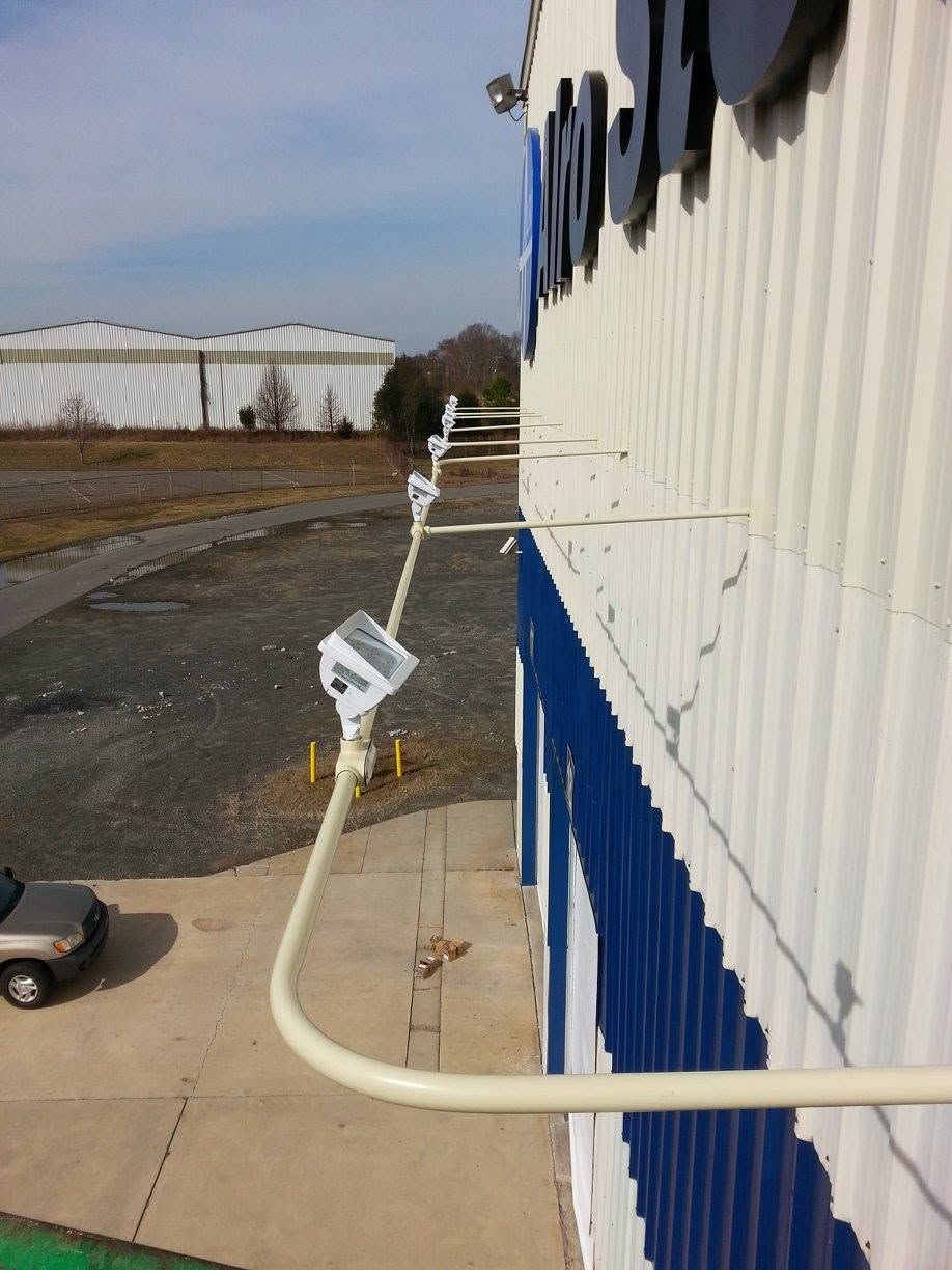 Exterior of a white industrial building with a blue lower wall and a mounted security camera on a sidewalk.