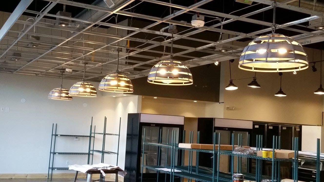Empty commercial interior with exposed ceiling grid, hanging lights, and shelving along the wall