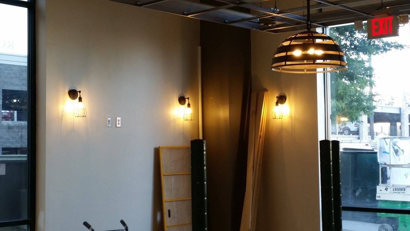 Modern interior with wall sconces, wood paneling, pendant lights, and large windows overlooking a street.