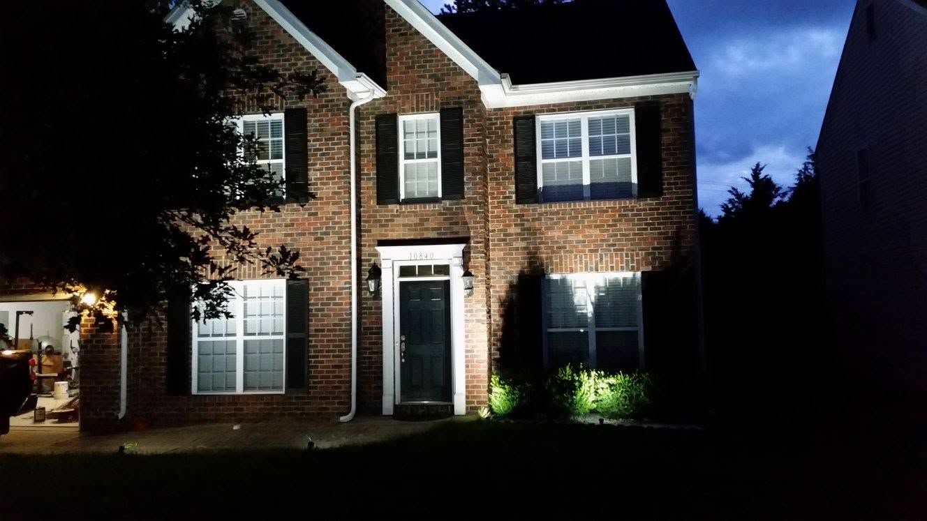 Brick house at night with lit windows, front door, and garage under a dark sky