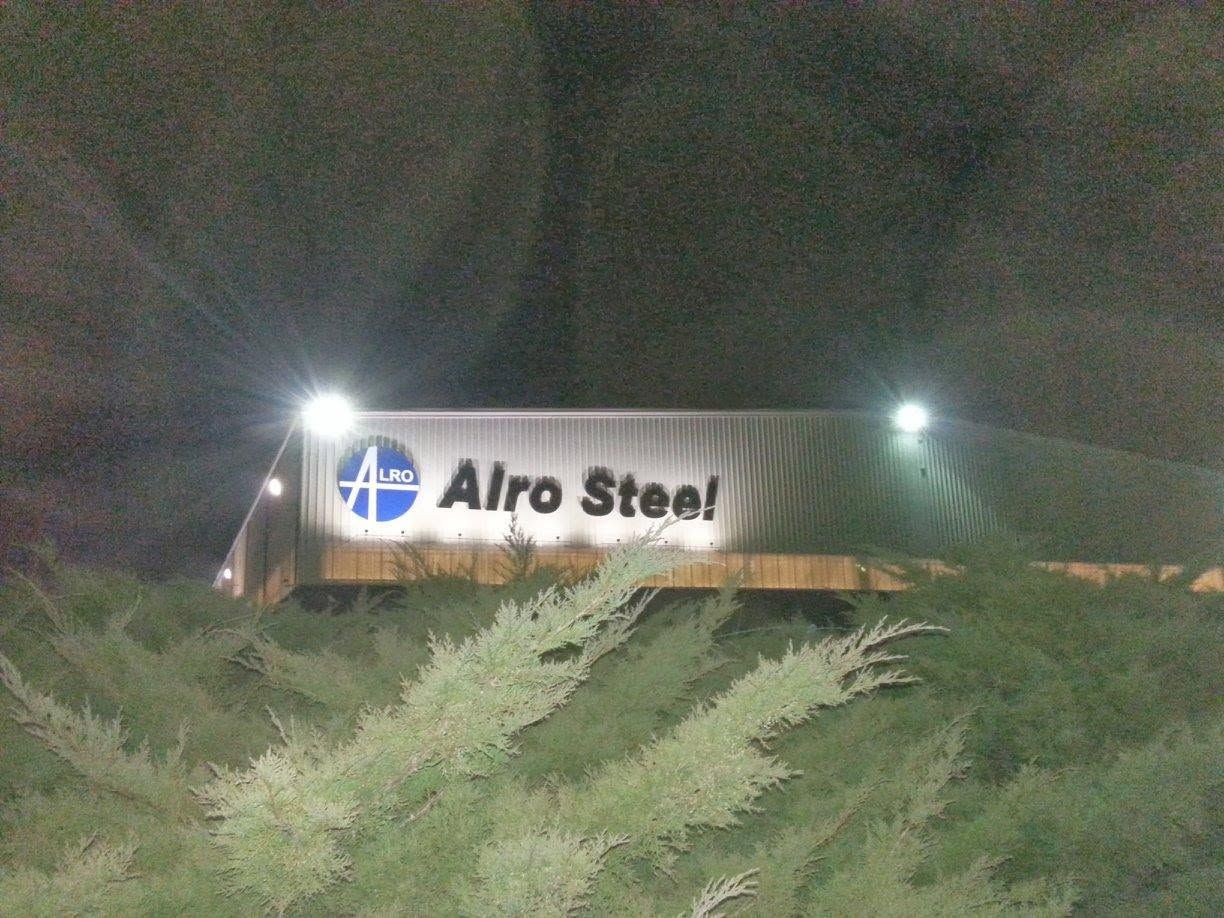 Airo Steel sign illuminated at night, viewed across brush with dark sky behind.